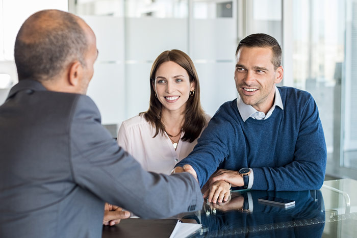 middle aged couple across the table from a man in a suit, the two men are shaking hands