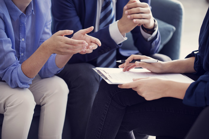closeup of the arms of a female taking notes on a clipboard with another female and male sitting across from her