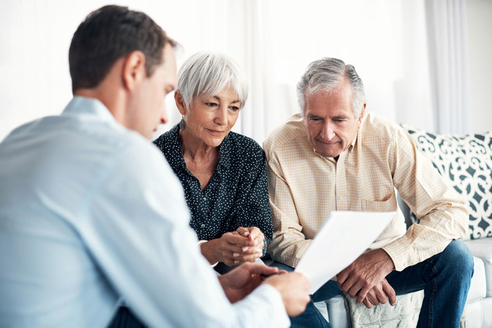 senior couple sitting down going over paperwork with business man